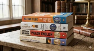 A stack of debut novels that won the Costa First Novel Award, including titles by British authors like Gail Honeyman and Nathan Filer on a rustic oak table.