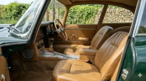 A close-up of the pristine tan leather bucket seats and centre console of a restored British sports car in natural afternoon light.